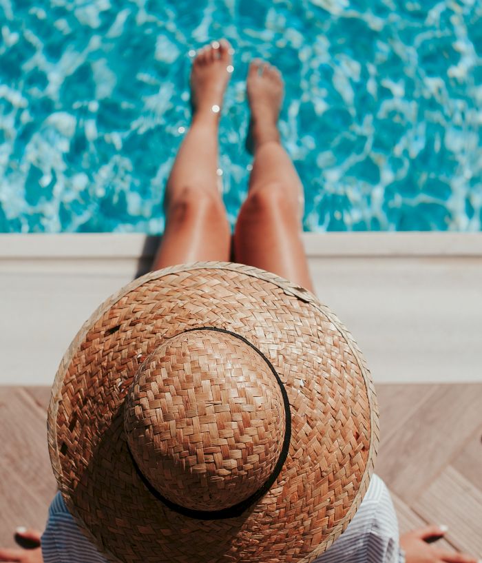 Relaxing poolside: sunhat on a towel, lying with bare feet in clear blue water.