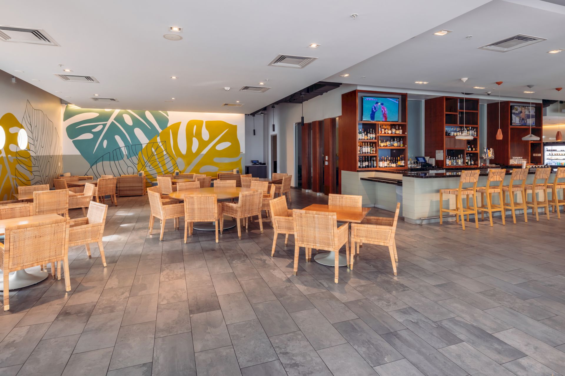 Modern restaurant lounge with a graffiti wall, rattan tables, a bar counter, and hanging lights for drinks and dining.
